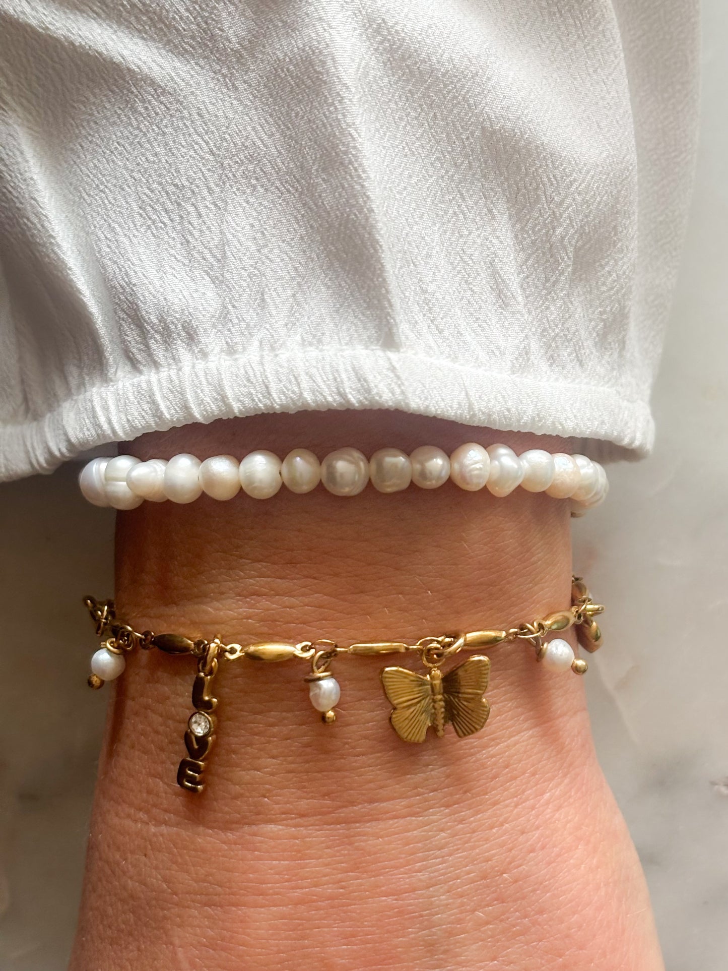 Pols met wit parel armbandje en rvs gouden bedel armband